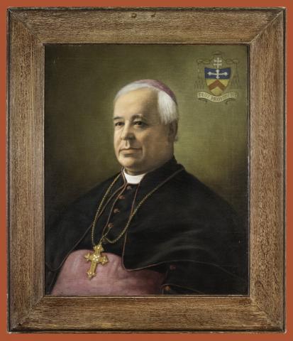 White haired man in ecclesiastical clothing with a crucifix around his neck.
