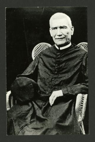 Photograph of a seated priest wearing a long black cassock.