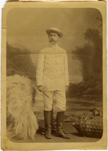 Full length photo of a man in a white riding suit wearing leather boots and carrying a riding crop.