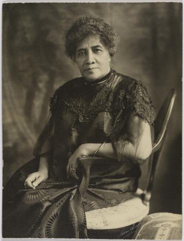 Sepia-tinted photo of a woman in a formal dress seated in a chair.