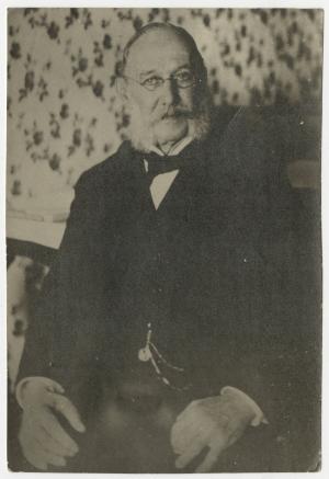Photo of a seated older man in a suit with a vest. He is balding with gray hair and muttonchops.