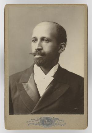 Bust length sepia-tinted photo of an African American man in a dark suit. He is balding with a moustache and trimmed beard.