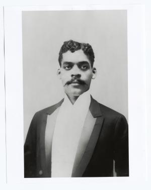 Waist length photo of a young man wearing a tuxedo. His hair is dark and he has a dark moustache.